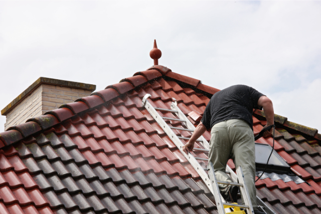 Man on a roof cleaning the tiles with pressure washer